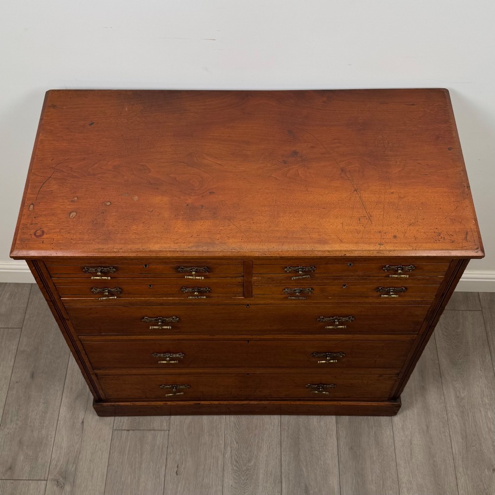 An antique walnut chest of drawers featuring decorative brass handles, reeded top drawer fronts, and a solid plinth base. View IX
