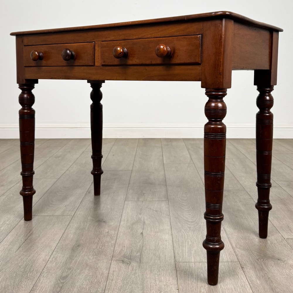 A Victorian mahogany writing table featuring two frieze drawers with wooden knobs and turned reeded legs. View II