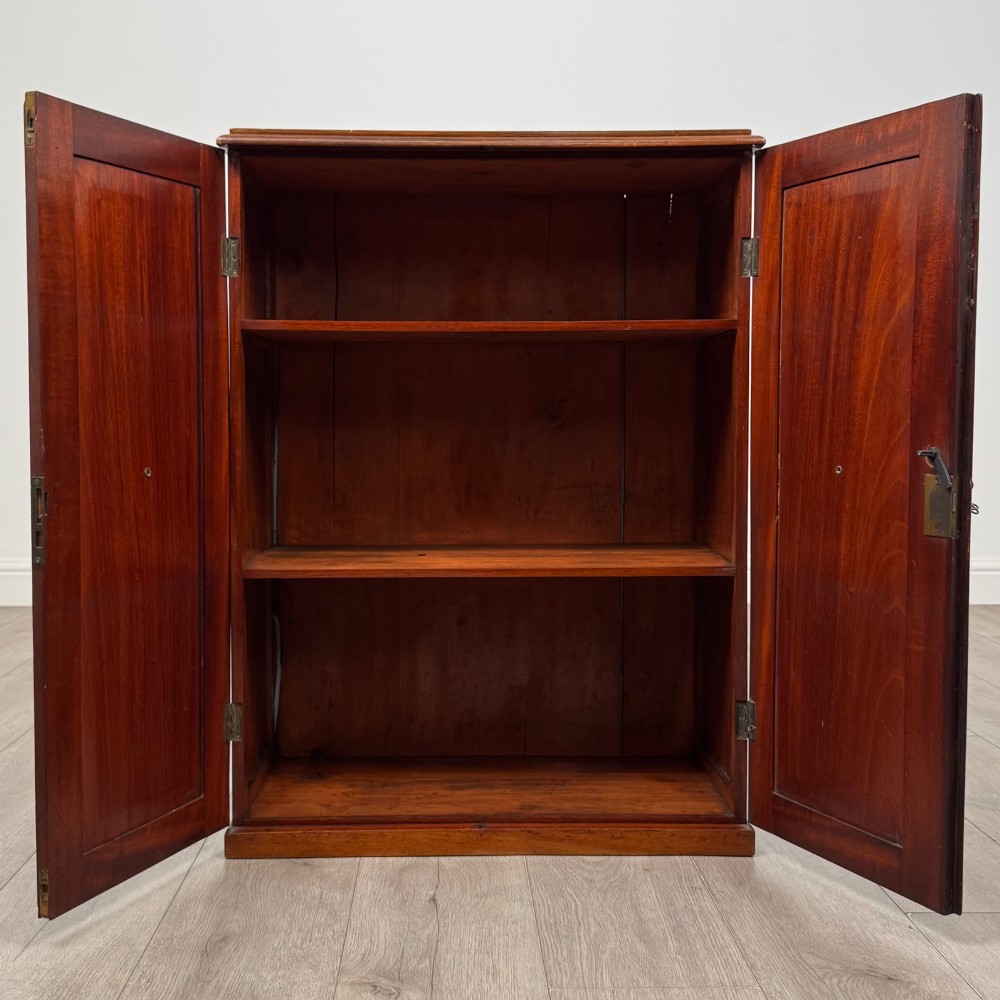 A small Victorian mahogany double-door cupboard featuring raised central panels, green circular brass flower mounts, and a decorative central keyhole. View II