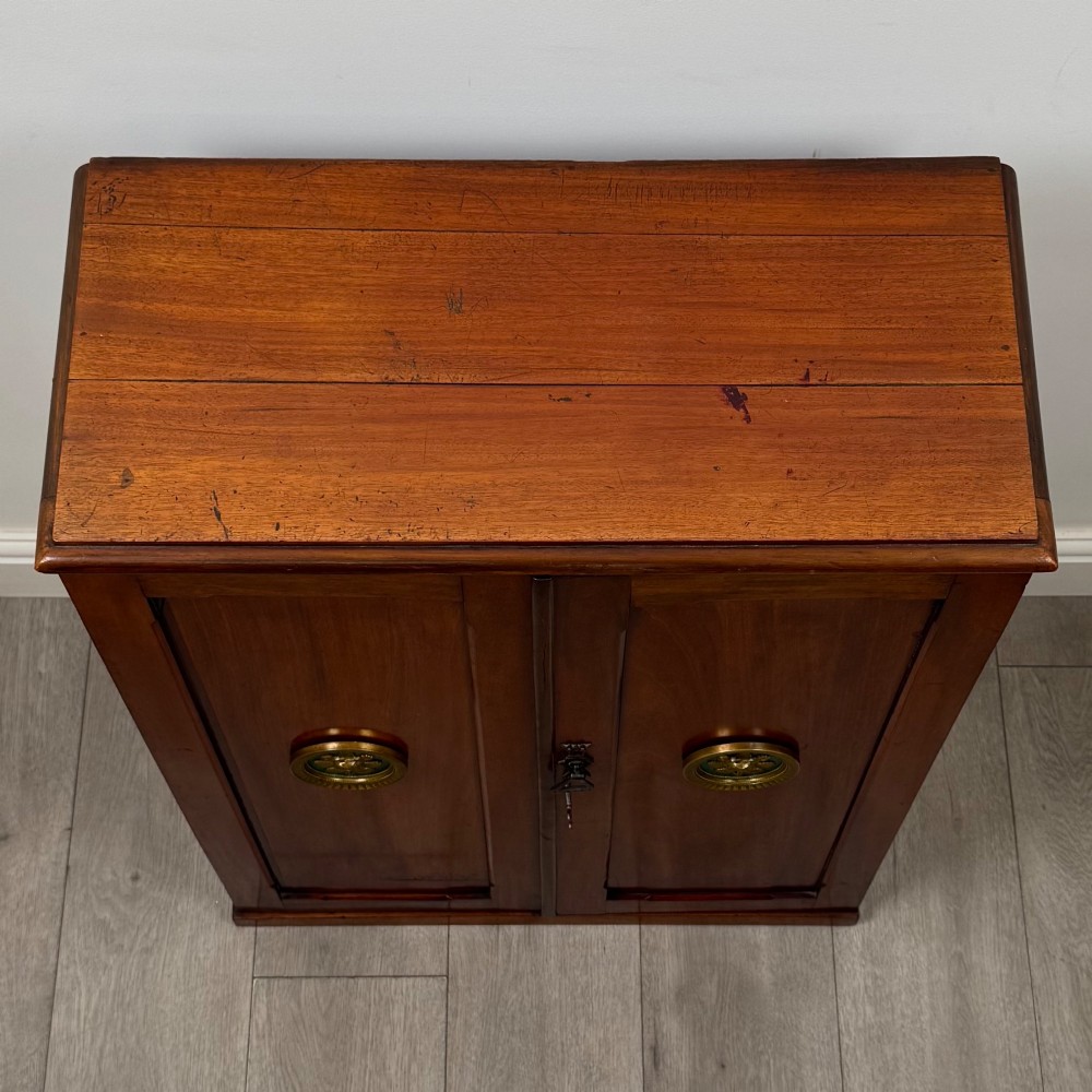 A small Victorian mahogany double-door cupboard featuring raised central panels, green circular brass flower mounts, and a decorative central keyhole. View X