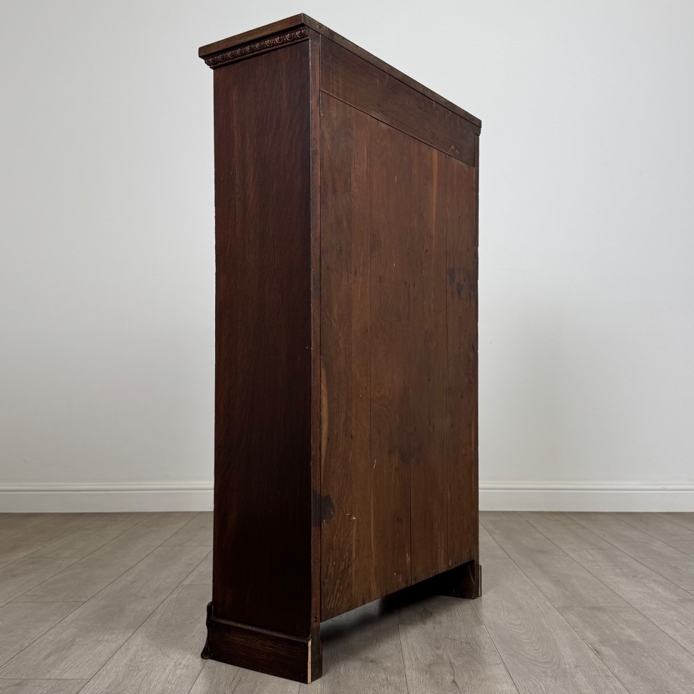 An Edwardian open oak bookcase featuring three interior fixed shelves, dark timber finish, carved moulding on top uprights, and a shaped plinth base. View V
