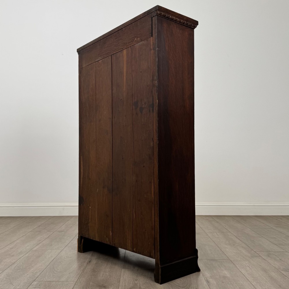 An Edwardian open oak bookcase featuring three interior fixed shelves, dark timber finish, carved moulding on top uprights, and a shaped plinth base. View VII