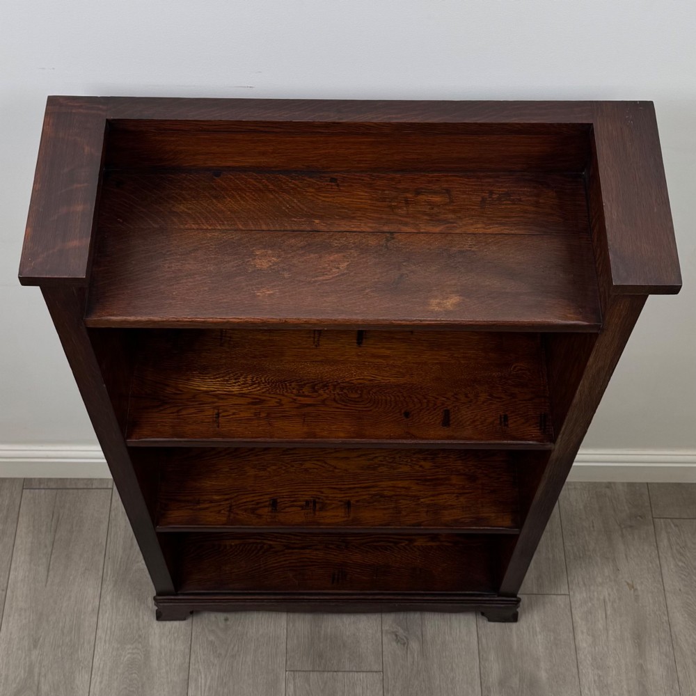 An Edwardian open oak bookcase featuring three interior fixed shelves, dark timber finish, carved moulding on top uprights, and a shaped plinth base. View X