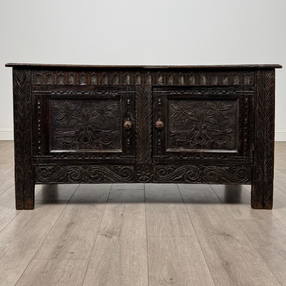 A low dark oak Victorian cupboard featuring two doors with relief carvings of birds and flowers, flanked by leafy carved uprights and a carved frieze.