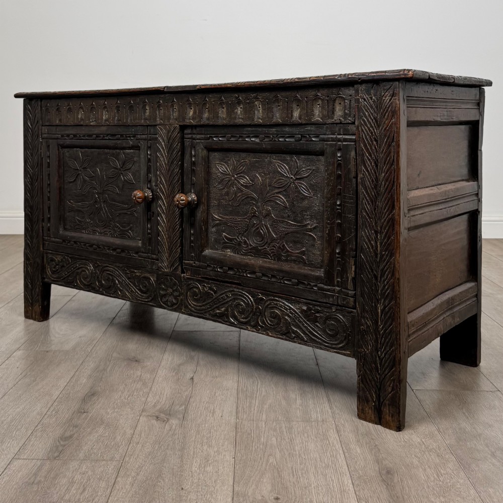 A low dark oak Victorian cupboard featuring two doors with relief carvings of birds and flowers, flanked by leafy carved uprights and a carved frieze. View III