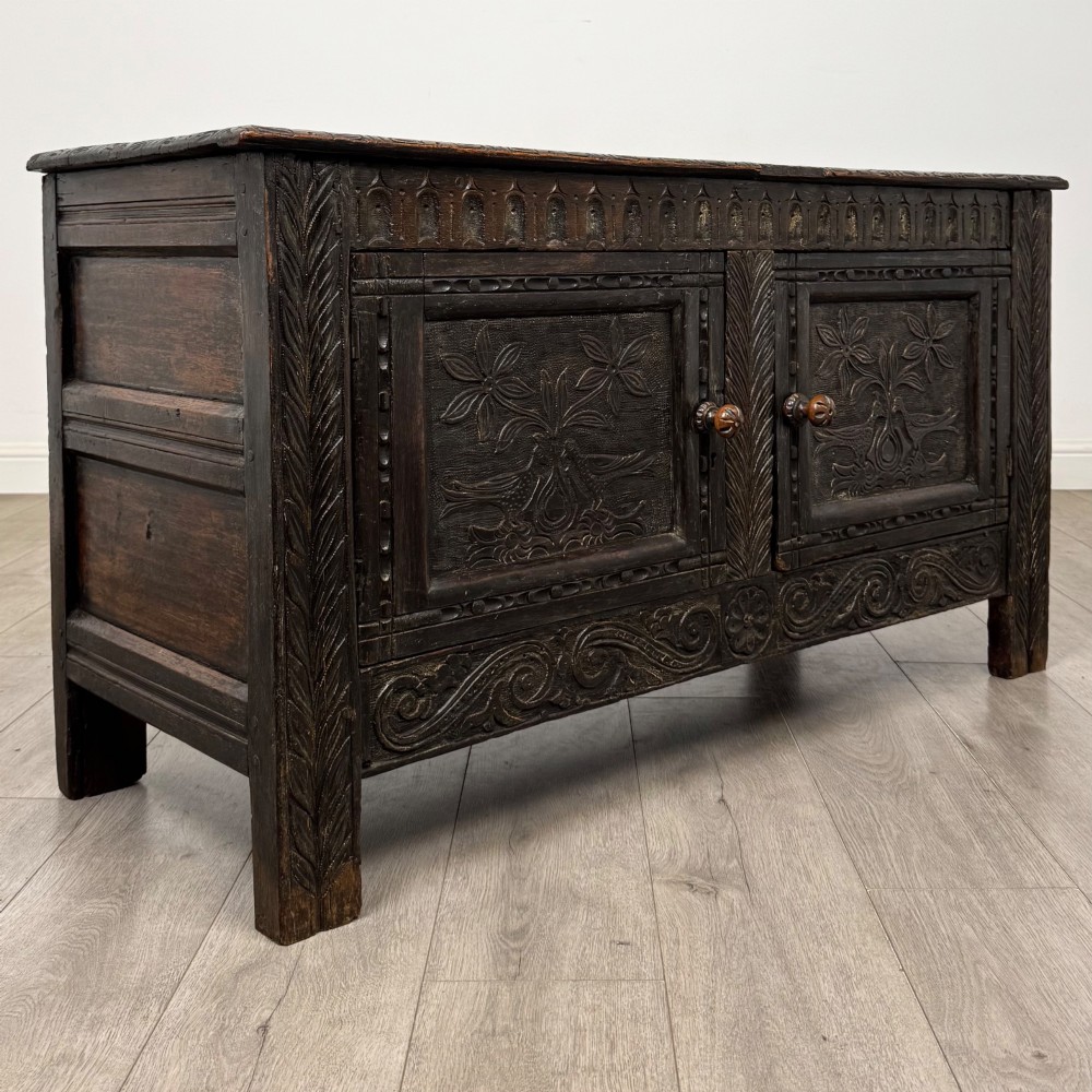 A low dark oak Victorian cupboard featuring two doors with relief carvings of birds and flowers, flanked by leafy carved uprights and a carved frieze. View IX