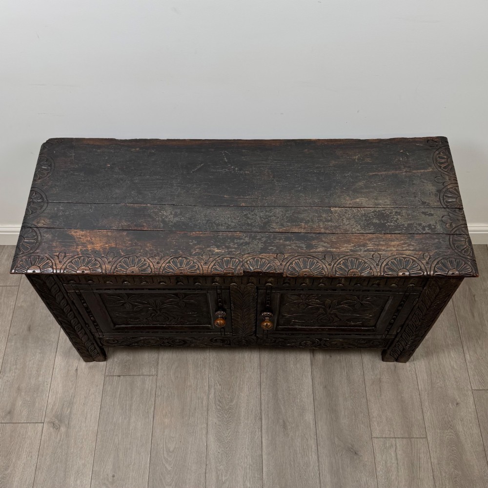 A low dark oak Victorian cupboard featuring two doors with relief carvings of birds and flowers, flanked by leafy carved uprights and a carved frieze. View X