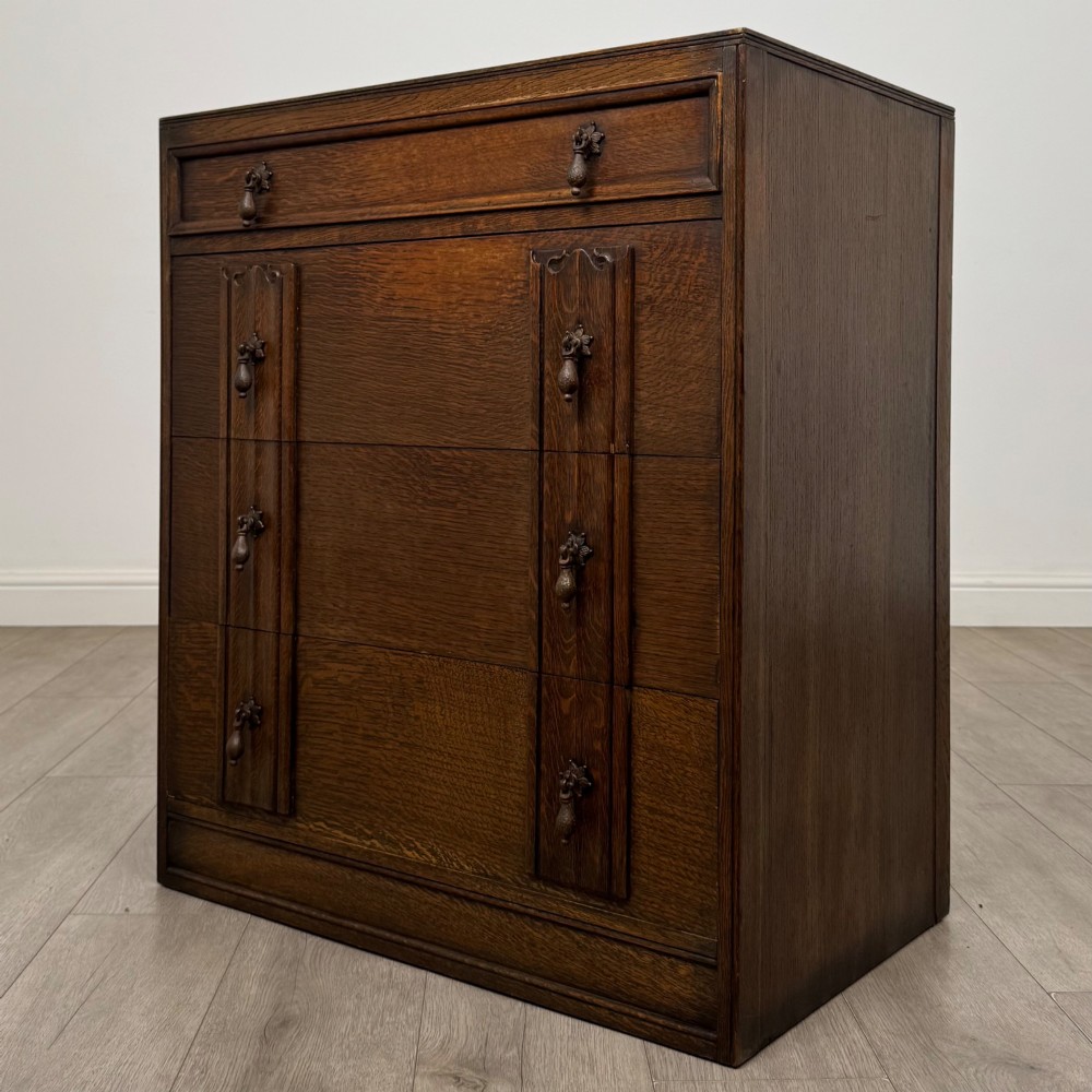 A dark oak chest of drawers featuring carved vertical linenfold panels and metallic drop handles. View II