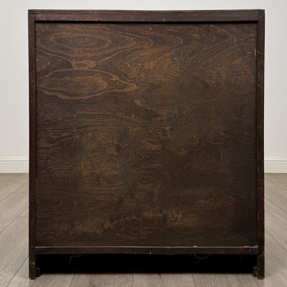 A dark oak chest of drawers featuring carved vertical linenfold panels and metallic drop handles. View V