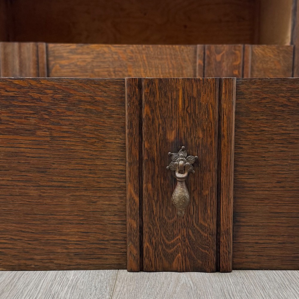 A dark oak chest of drawers featuring carved vertical linenfold panels and metallic drop handles. View XI