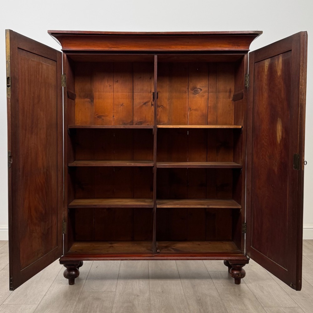 An antique Victorian mahogany storage cabinet featuring two panelled doors, turned bun feet, and a classic moulded top cornicing. View II