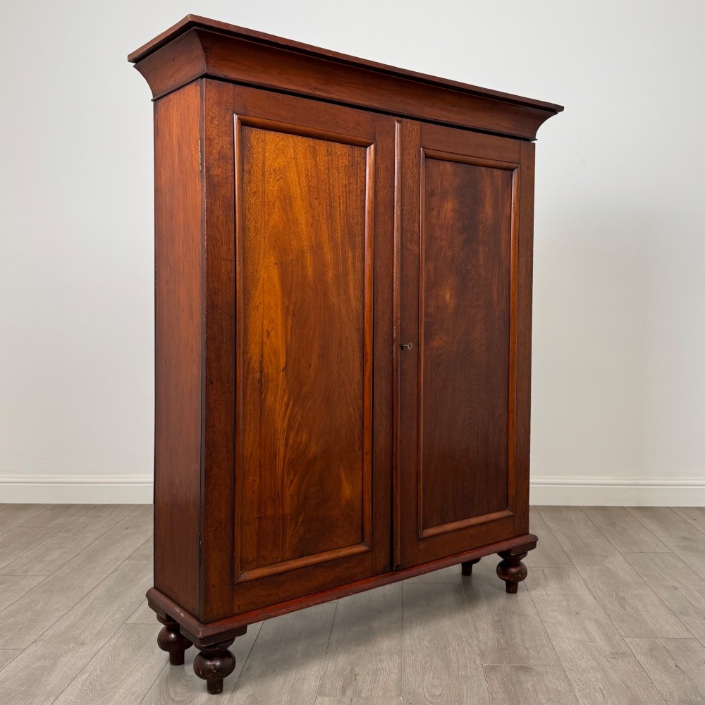 An antique Victorian mahogany storage cabinet featuring two panelled doors, turned bun feet, and a classic moulded top cornicing. View IX