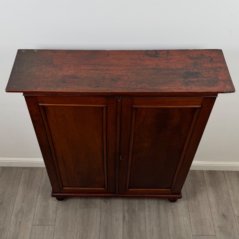 An antique Victorian mahogany storage cabinet featuring two panelled doors, turned bun feet, and a classic moulded top cornicing. View X