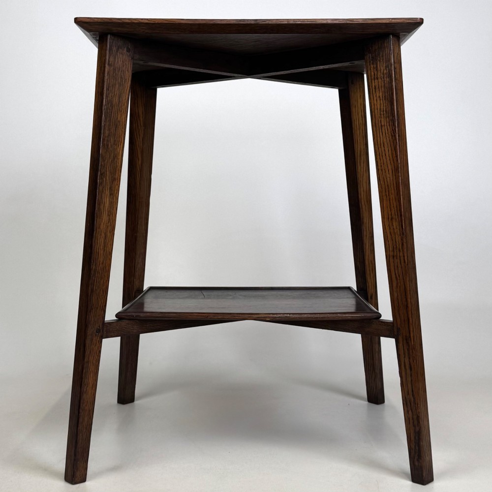 An Edwardian dark oak side table featuring a square top, cross-stretchers, tapered legs, and a lower square shelf.