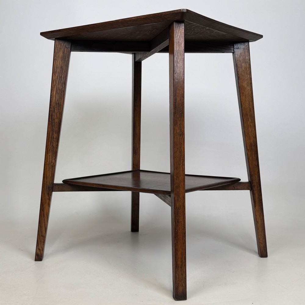 An Edwardian dark oak side table featuring a square top, cross-stretchers, tapered legs, and a lower square shelf. View VI
