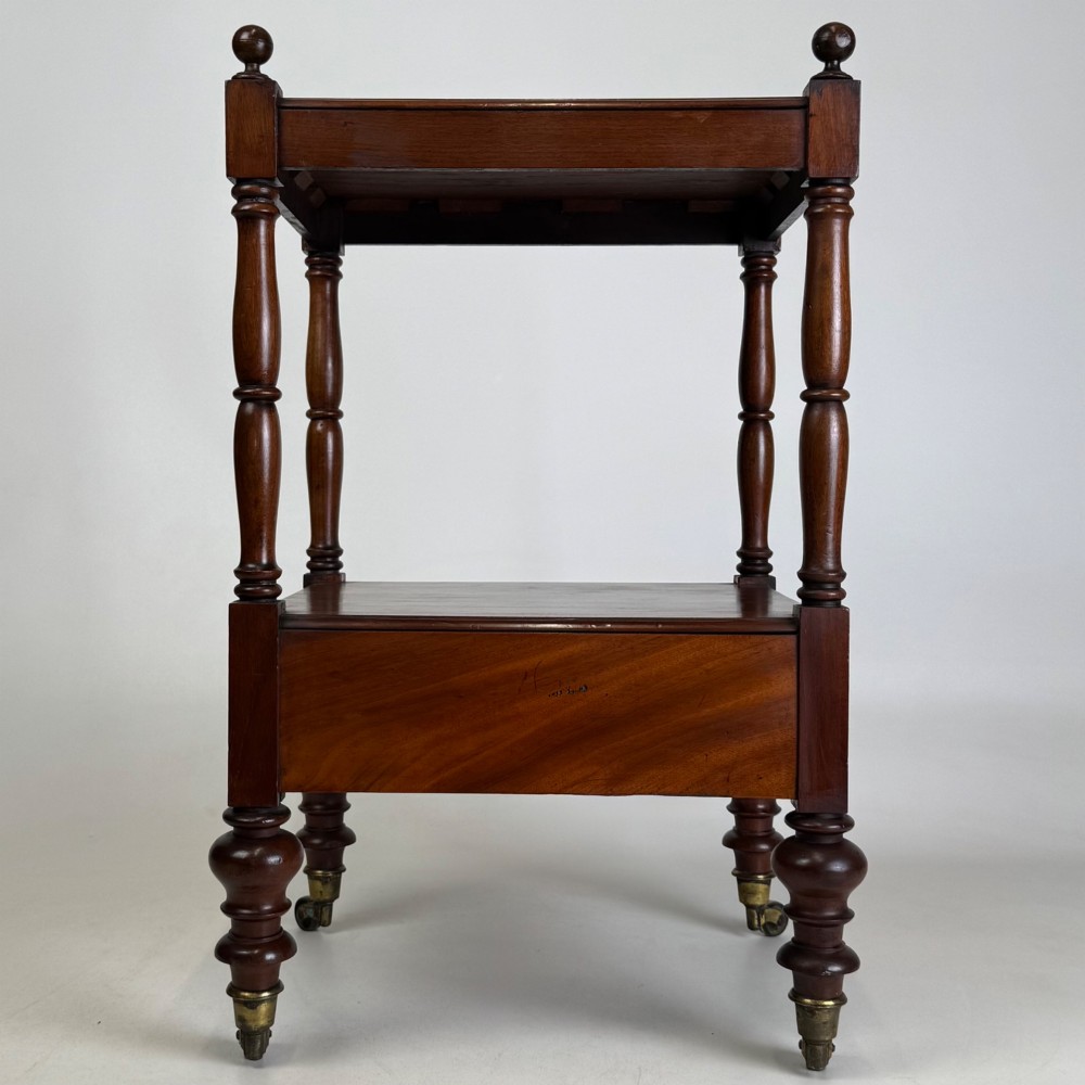 A Victorian mahogany two-tiered stand featuring turned corner supports, top finials, a lower single drawer with a round wooden knob, and brass castors. View V