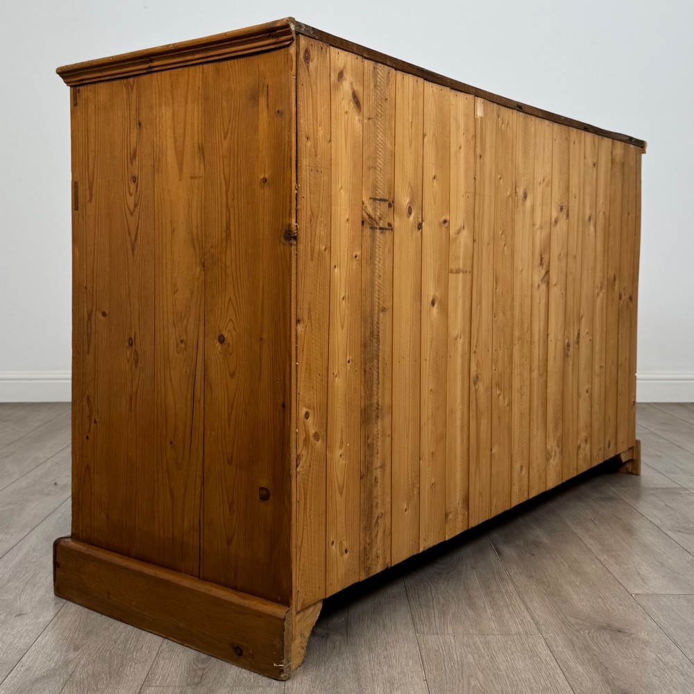 A vintage pine farmhouse sideboard featuring three frieze drawers above three panelled cupboard doors with turned wooden knobs on a plinth base. View V