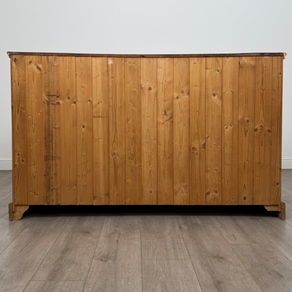 A vintage pine farmhouse sideboard featuring three frieze drawers above three panelled cupboard doors with turned wooden knobs on a plinth base. View VI