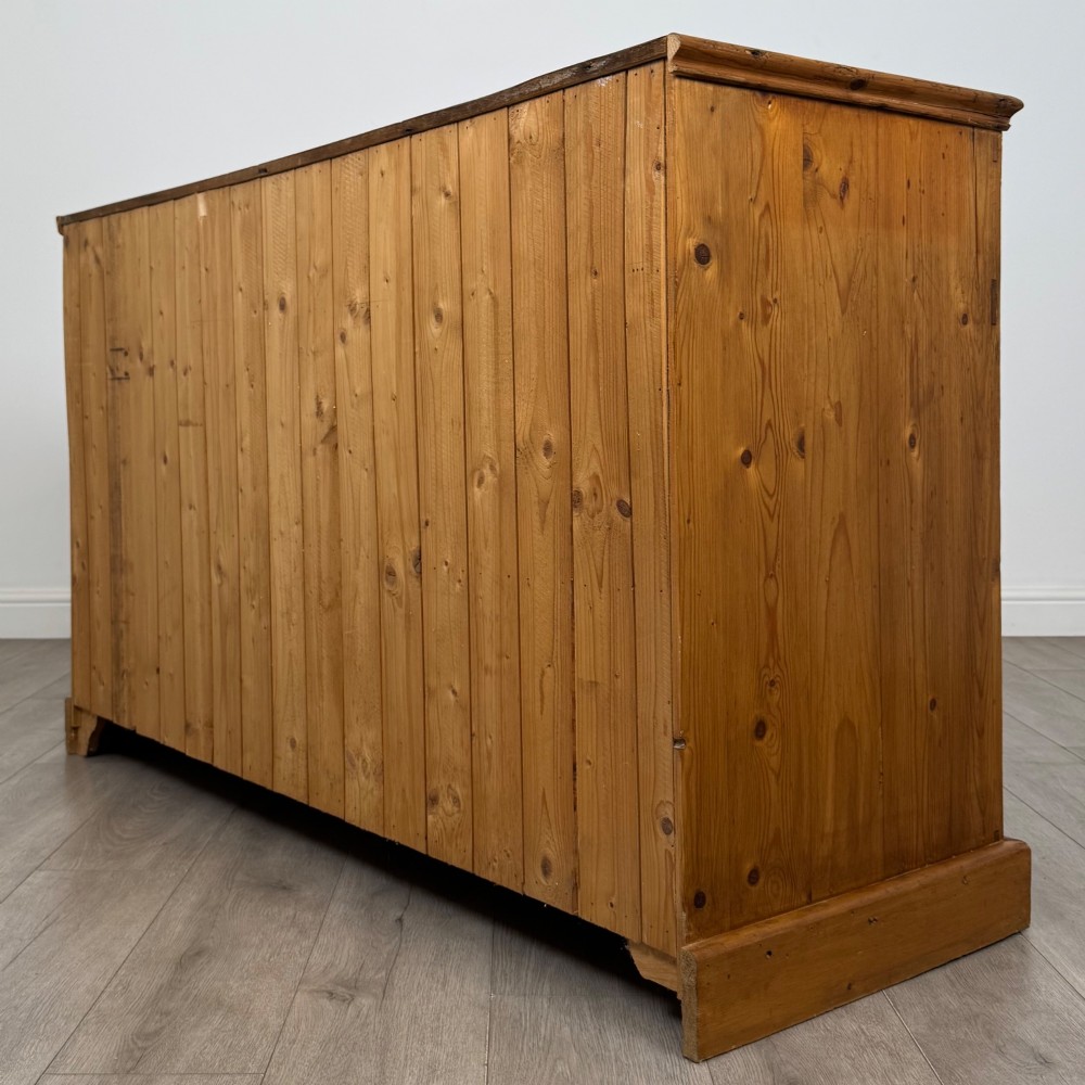 A vintage pine farmhouse sideboard featuring three frieze drawers above three panelled cupboard doors with turned wooden knobs on a plinth base. View VII