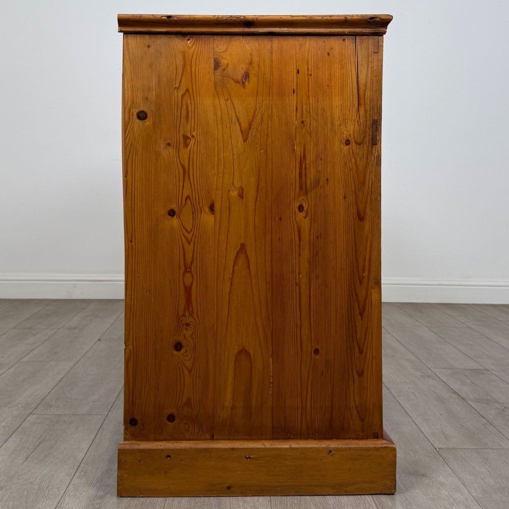A vintage pine farmhouse sideboard featuring three frieze drawers above three panelled cupboard doors with turned wooden knobs on a plinth base. View VIII