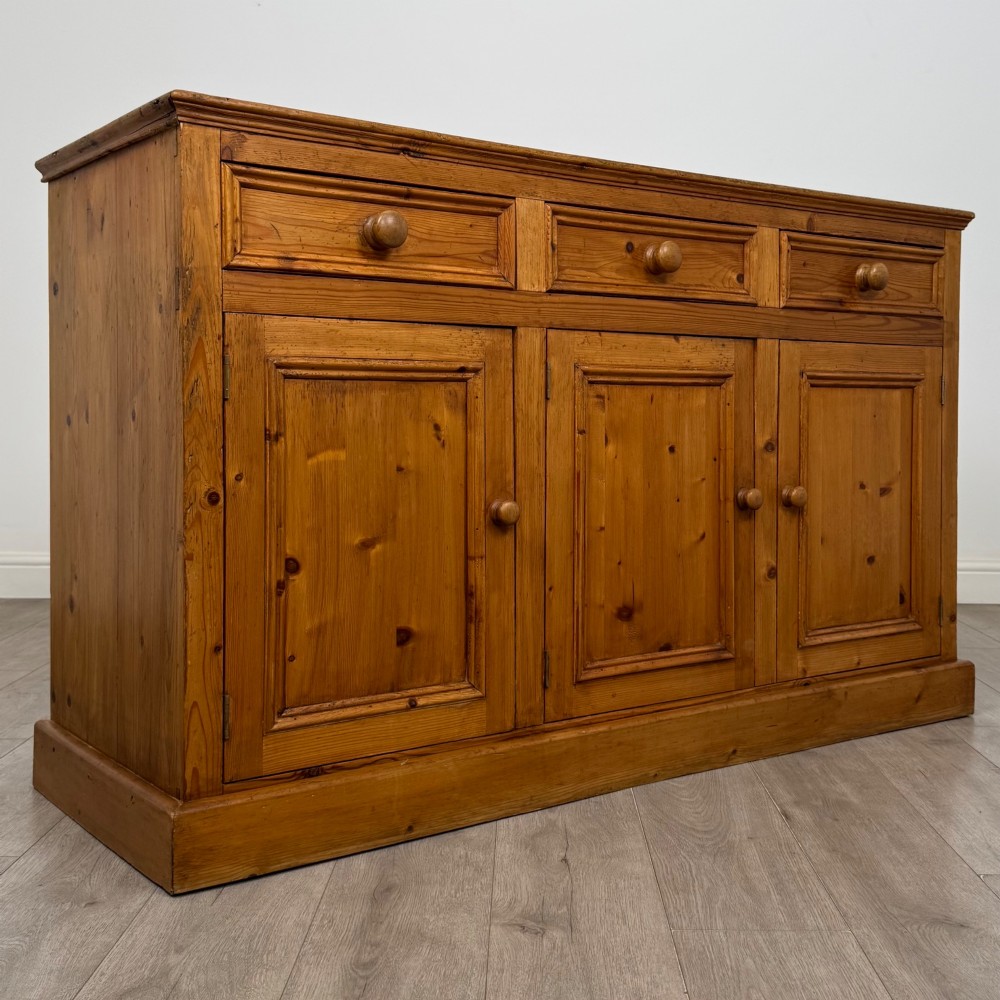A vintage pine farmhouse sideboard featuring three frieze drawers above three panelled cupboard doors with turned wooden knobs on a plinth base. View IX