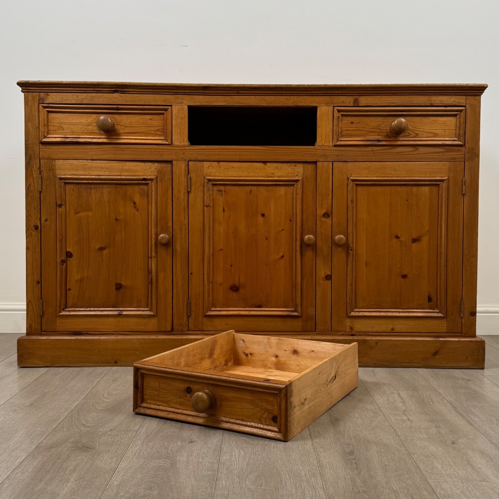 A vintage pine farmhouse sideboard featuring three frieze drawers above three panelled cupboard doors with turned wooden knobs on a plinth base. View XI
