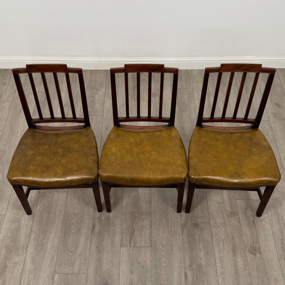 A set of six antique mahogany dining chairs featuring vertical slat backs, square legs, and olive green leather seats finished with brass studs. View VIII