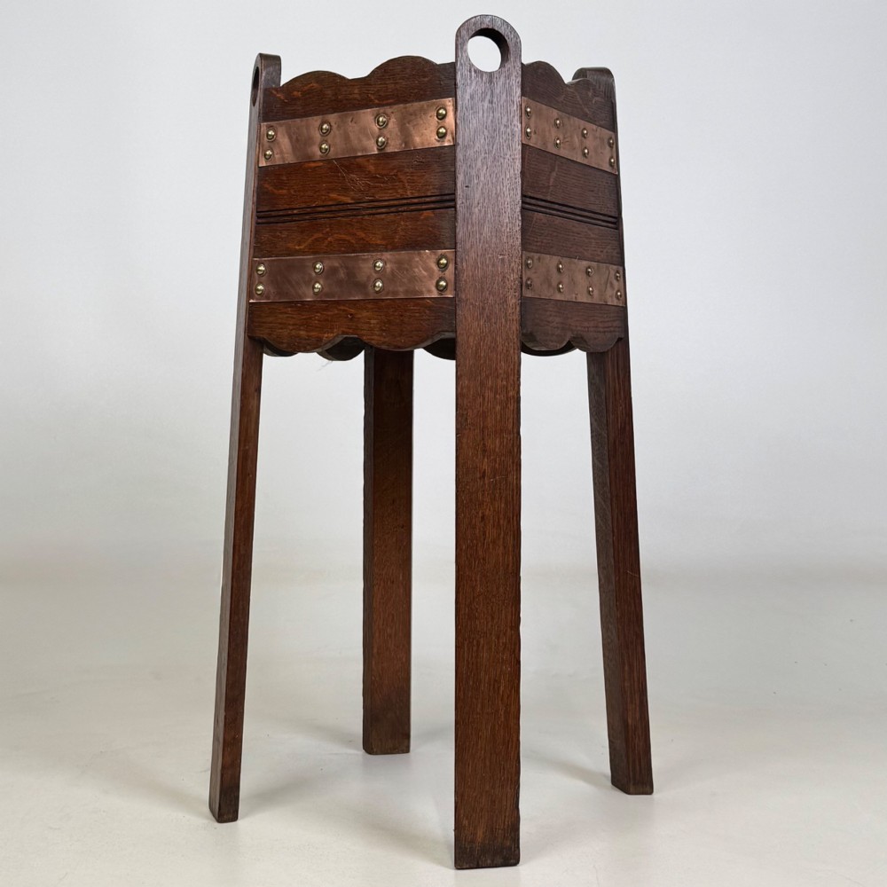 An antique Arts and Crafts dark oak plant stand featuring copper straps with brass rivets, pierced handles, and scalloped edges. View II
