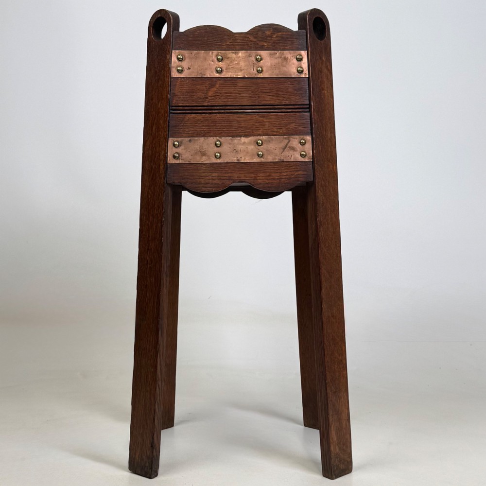 An antique Arts and Crafts dark oak plant stand featuring copper straps with brass rivets, pierced handles, and scalloped edges. View III