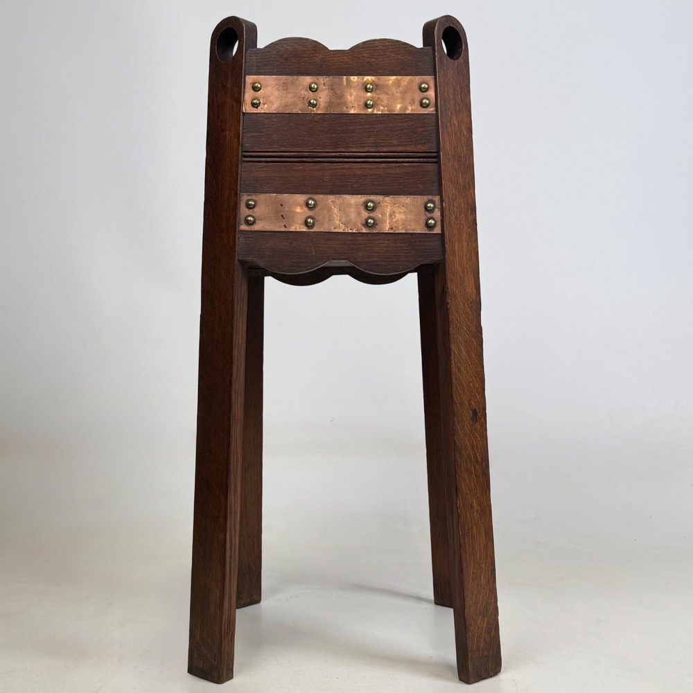 An antique Arts and Crafts dark oak plant stand featuring copper straps with brass rivets, pierced handles, and scalloped edges. View V