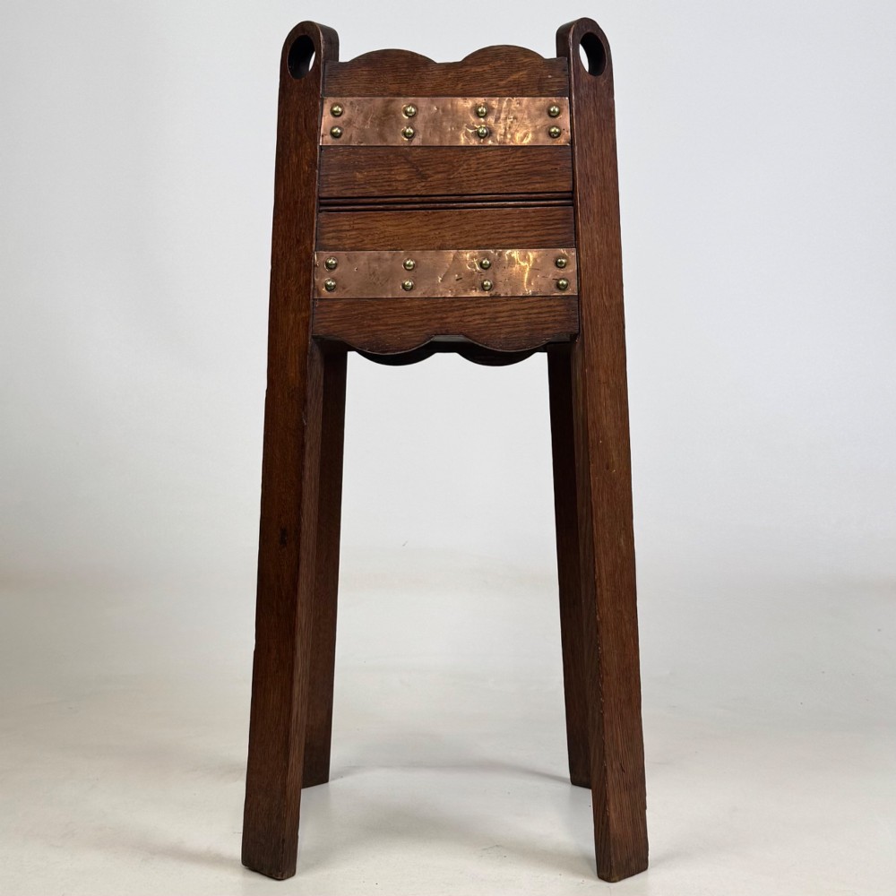 An antique Arts and Crafts dark oak plant stand featuring copper straps with brass rivets, pierced handles, and scalloped edges. View VII
