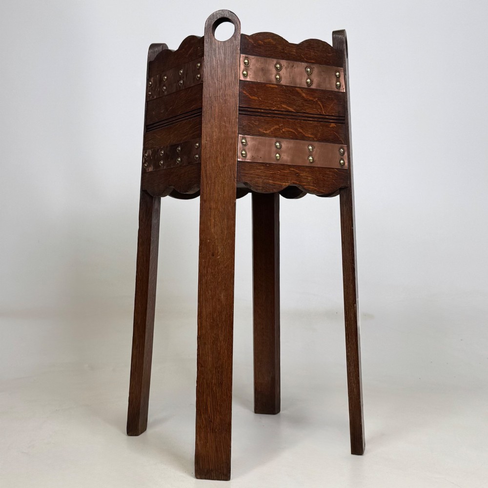 An antique Arts and Crafts dark oak plant stand featuring copper straps with brass rivets, pierced handles, and scalloped edges. View VIII