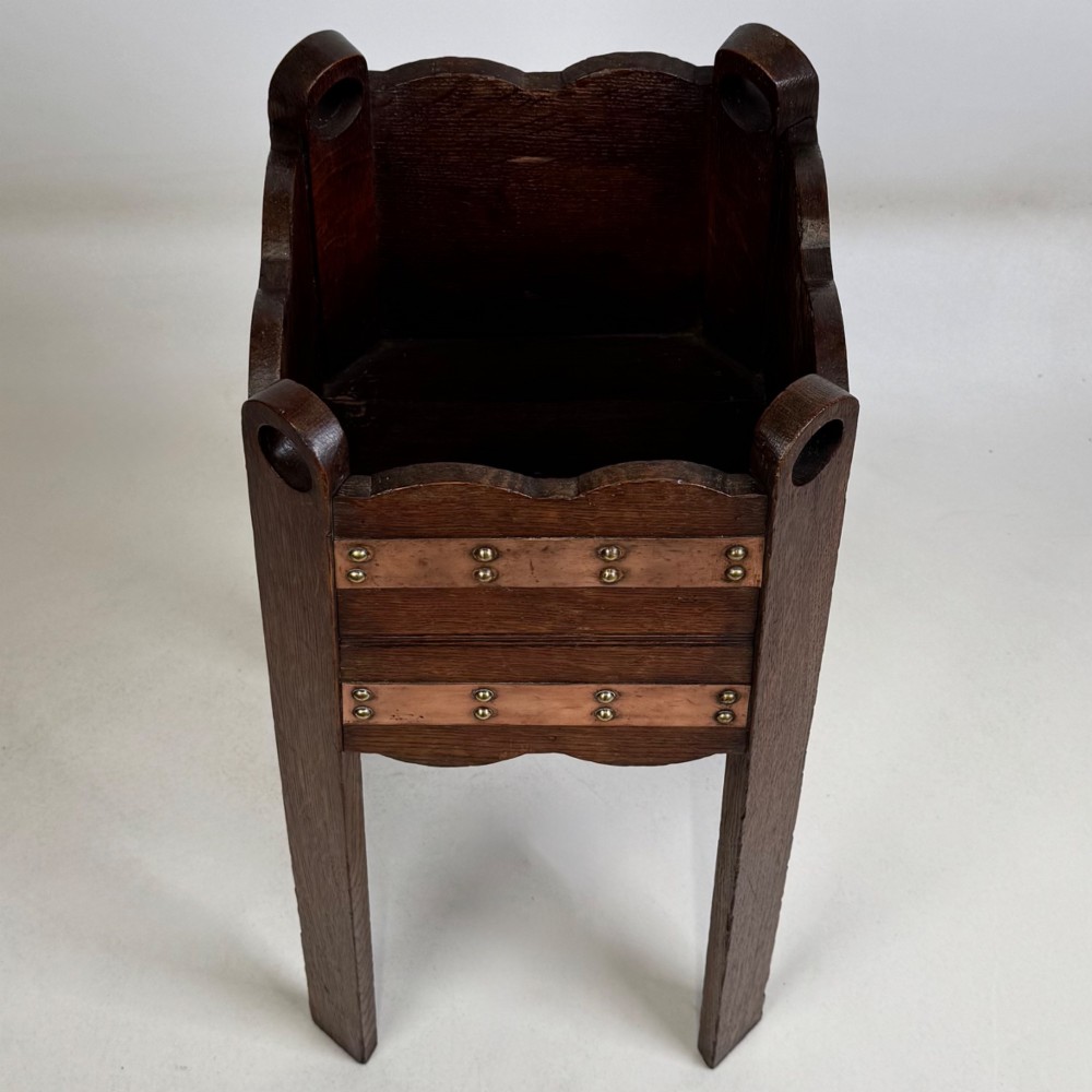 An antique Arts and Crafts dark oak plant stand featuring copper straps with brass rivets, pierced handles, and scalloped edges. View IX
