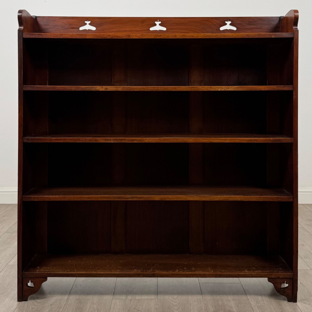 An early 20th-century Arts and Crafts open walnut bookcase featuring four shelves and decorative pierced cut-outs on the top gallery and plinth base. View II