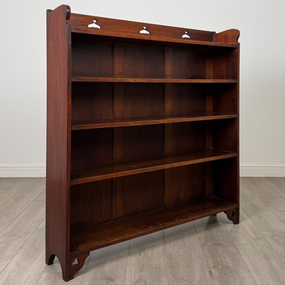 An early 20th-century Arts and Crafts open walnut bookcase featuring four shelves and decorative pierced cut-outs on the top gallery and plinth base. View IX