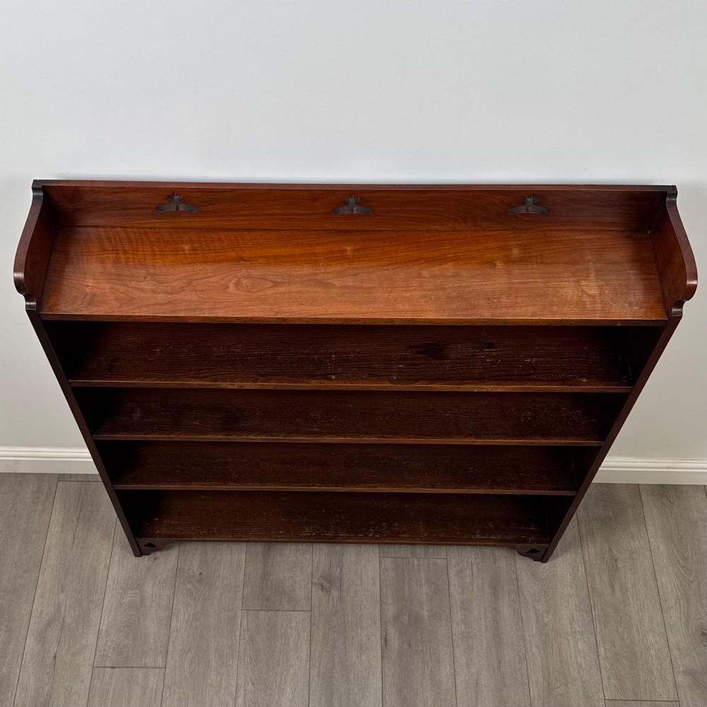 An early 20th-century Arts and Crafts open walnut bookcase featuring four shelves and decorative pierced cut-outs on the top gallery and plinth base. View X