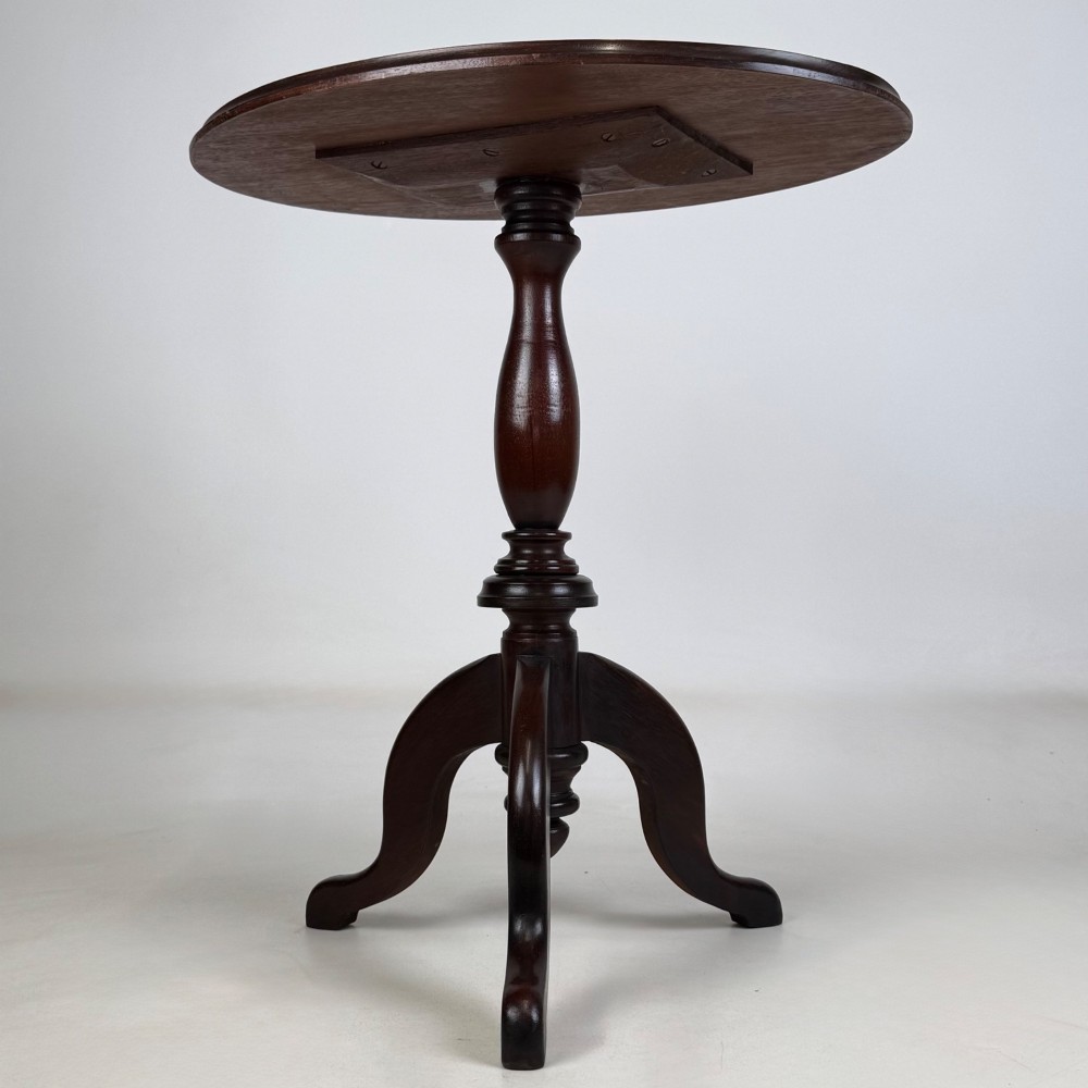 An antique dark mahogany side table featuring a smooth oval top, a centrally turned pedestal stem, and three splayed tripod legs.