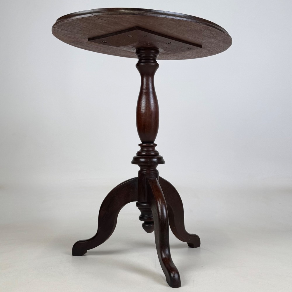 An antique dark mahogany side table featuring a smooth oval top, a centrally turned pedestal stem, and three splayed tripod legs. View IV