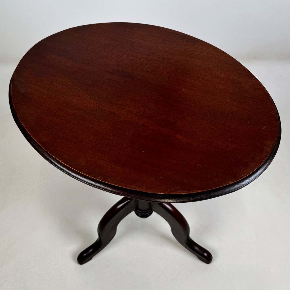 An antique dark mahogany side table featuring a smooth oval top, a centrally turned pedestal stem, and three splayed tripod legs. View V