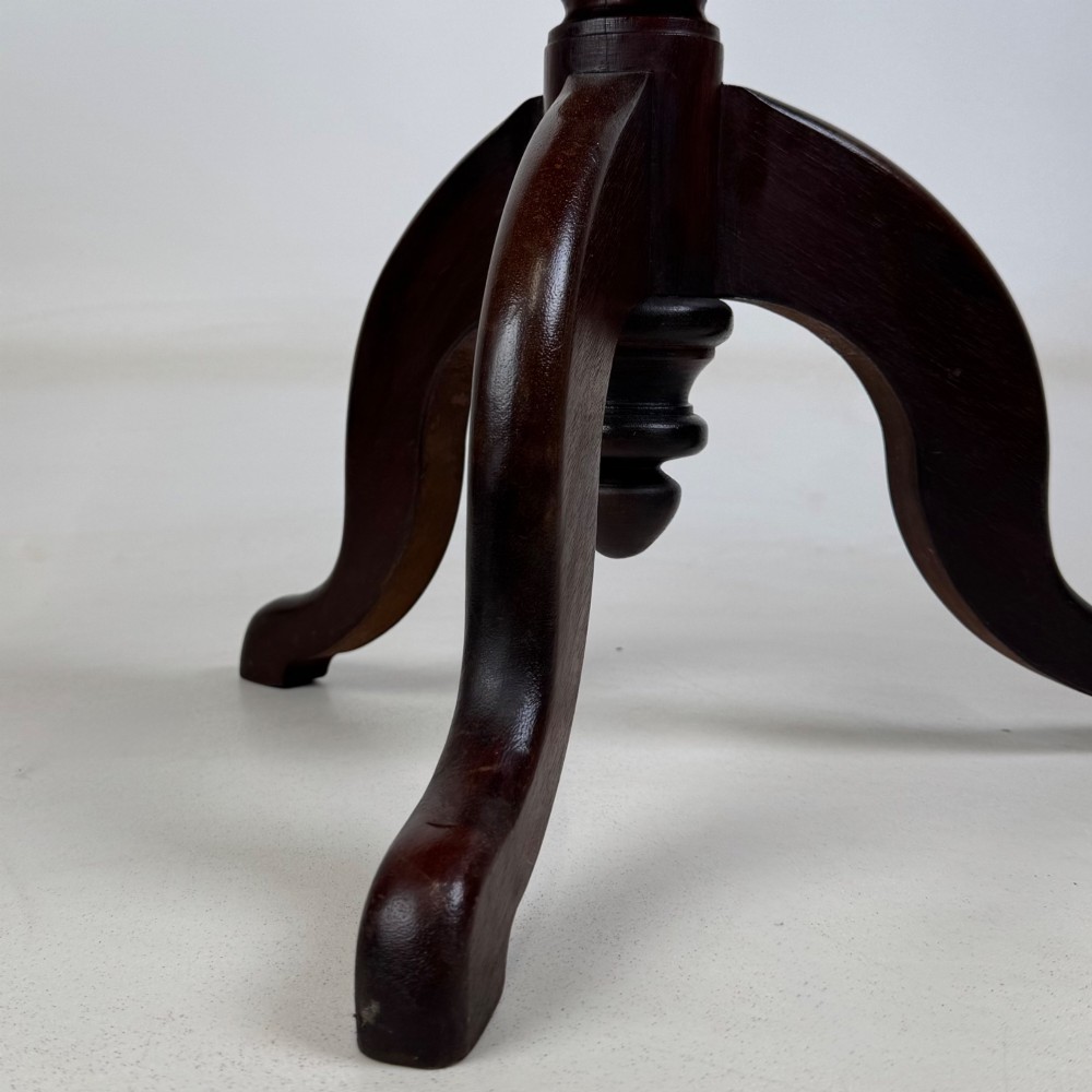An antique dark mahogany side table featuring a smooth oval top, a centrally turned pedestal stem, and three splayed tripod legs. View VI