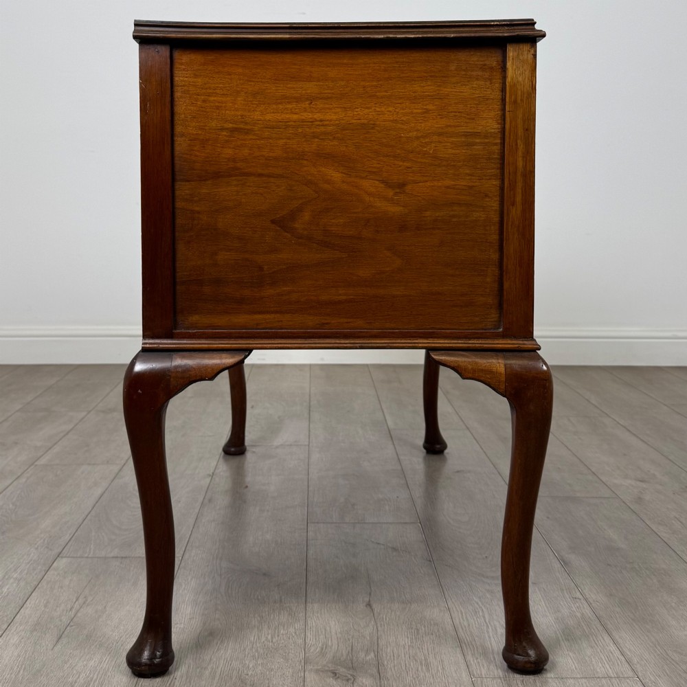 A 20th-century walnut writing table featuring four drawers, decorative brass drop handles, an arched kneehole centre, and curved cabriole legs. View VII