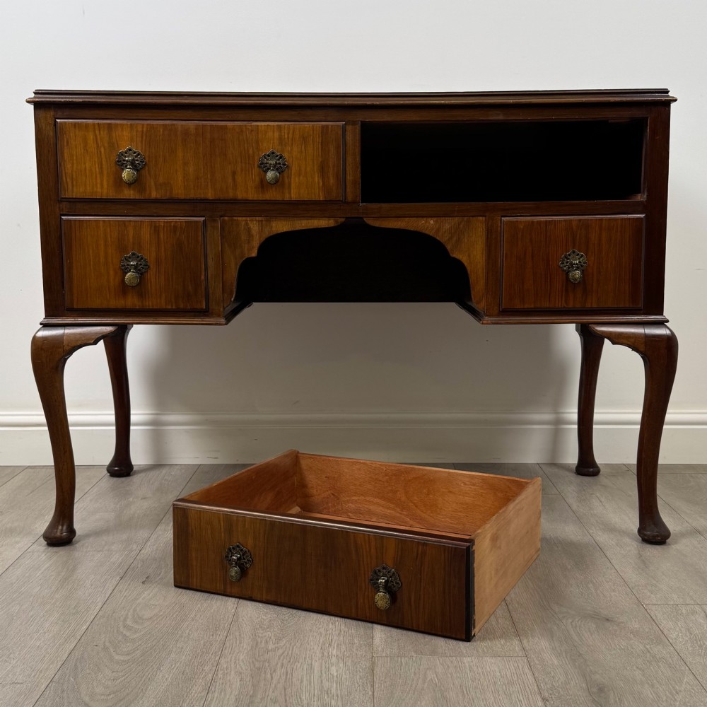 A 20th-century walnut writing table featuring four drawers, decorative brass drop handles, an arched kneehole centre, and curved cabriole legs. View X