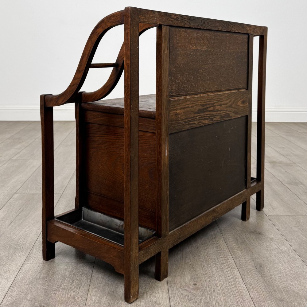 An antique Edwardian golden oak hall seat featuring a central panelled backrest and integrated side umbrella stands with metal drip trays. View IV