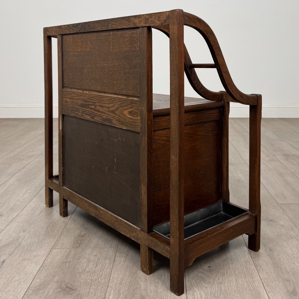 An antique Edwardian golden oak hall seat featuring a central panelled backrest and integrated side umbrella stands with metal drip trays. View VI