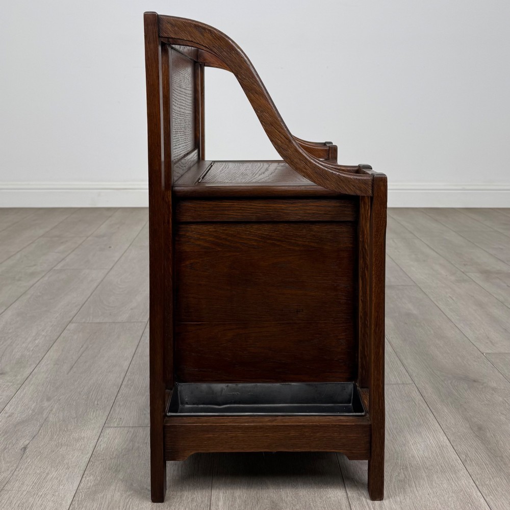 An antique Edwardian golden oak hall seat featuring a central panelled backrest and integrated side umbrella stands with metal drip trays. View VII
