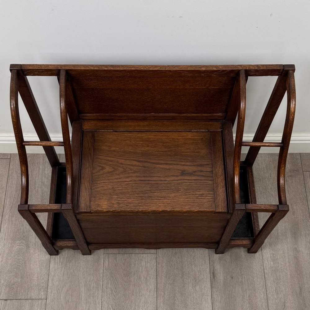 An antique Edwardian golden oak hall seat featuring a central panelled backrest and integrated side umbrella stands with metal drip trays. View IX