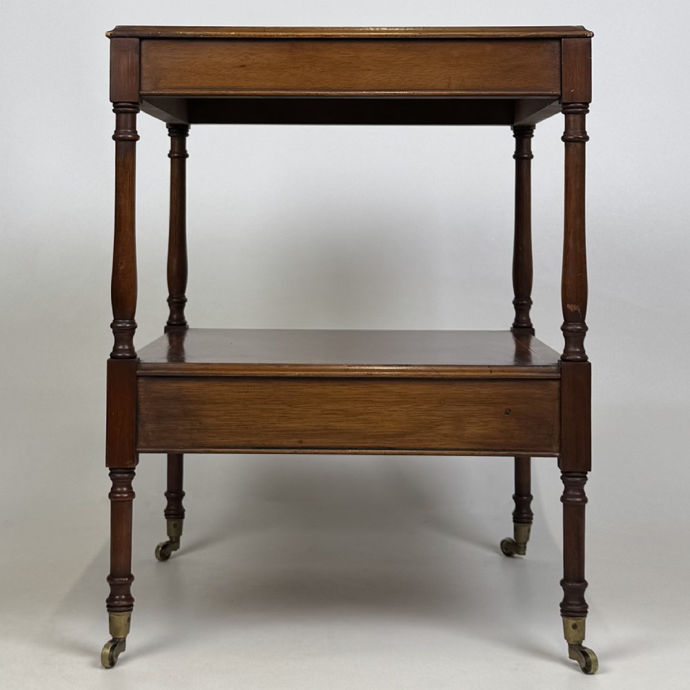 A pair of 20th-century warm mahogany bedside tables featuring turned support pillars, open middle shelves, single lower drawers with brass handles, and brass castors. View VI