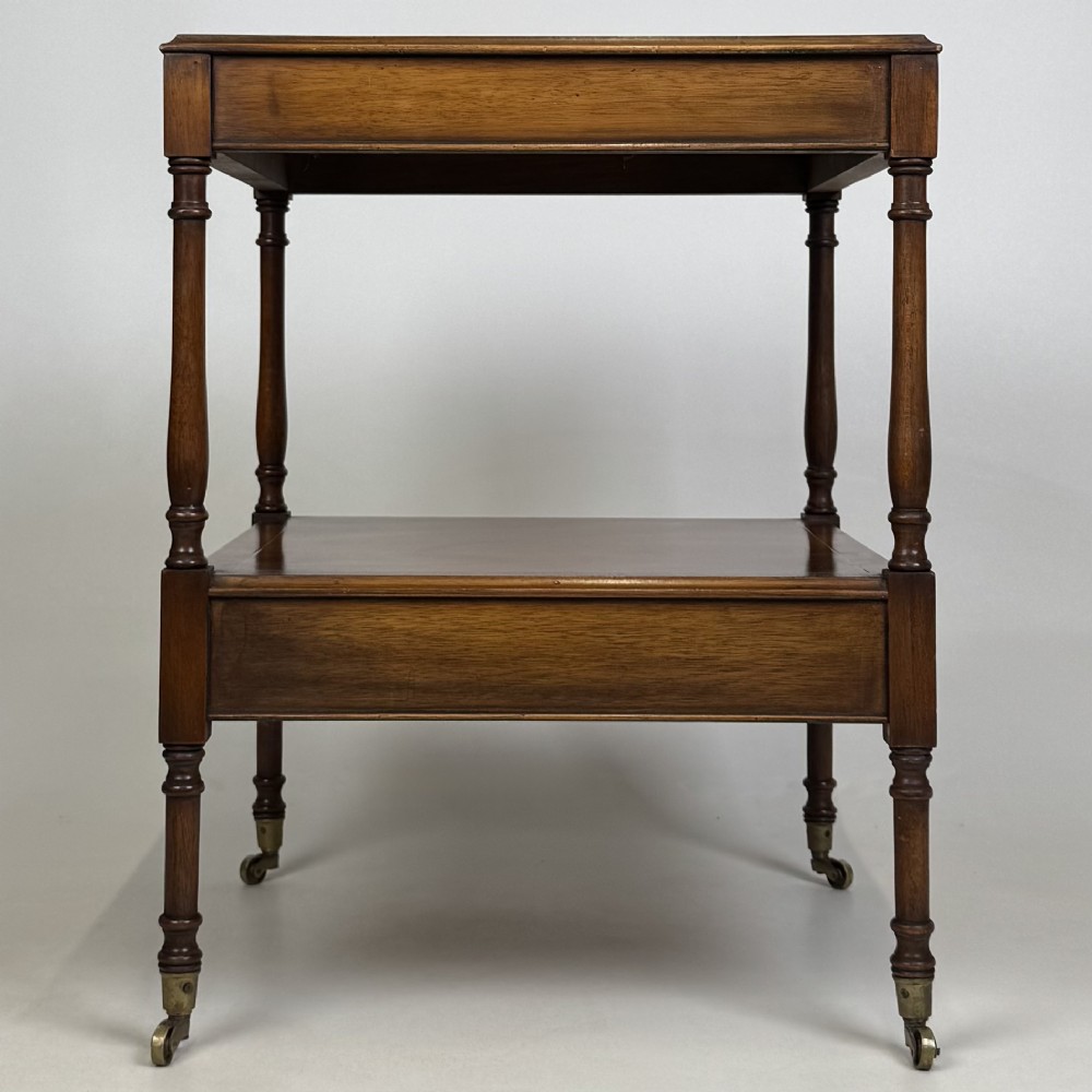 A pair of 20th-century warm mahogany bedside tables featuring turned support pillars, open middle shelves, single lower drawers with brass handles, and brass castors. View VIII