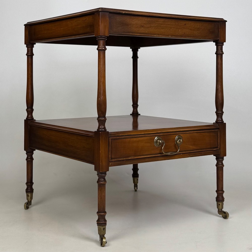 A pair of 20th-century warm mahogany bedside tables featuring turned support pillars, open middle shelves, single lower drawers with brass handles, and brass castors. View IX