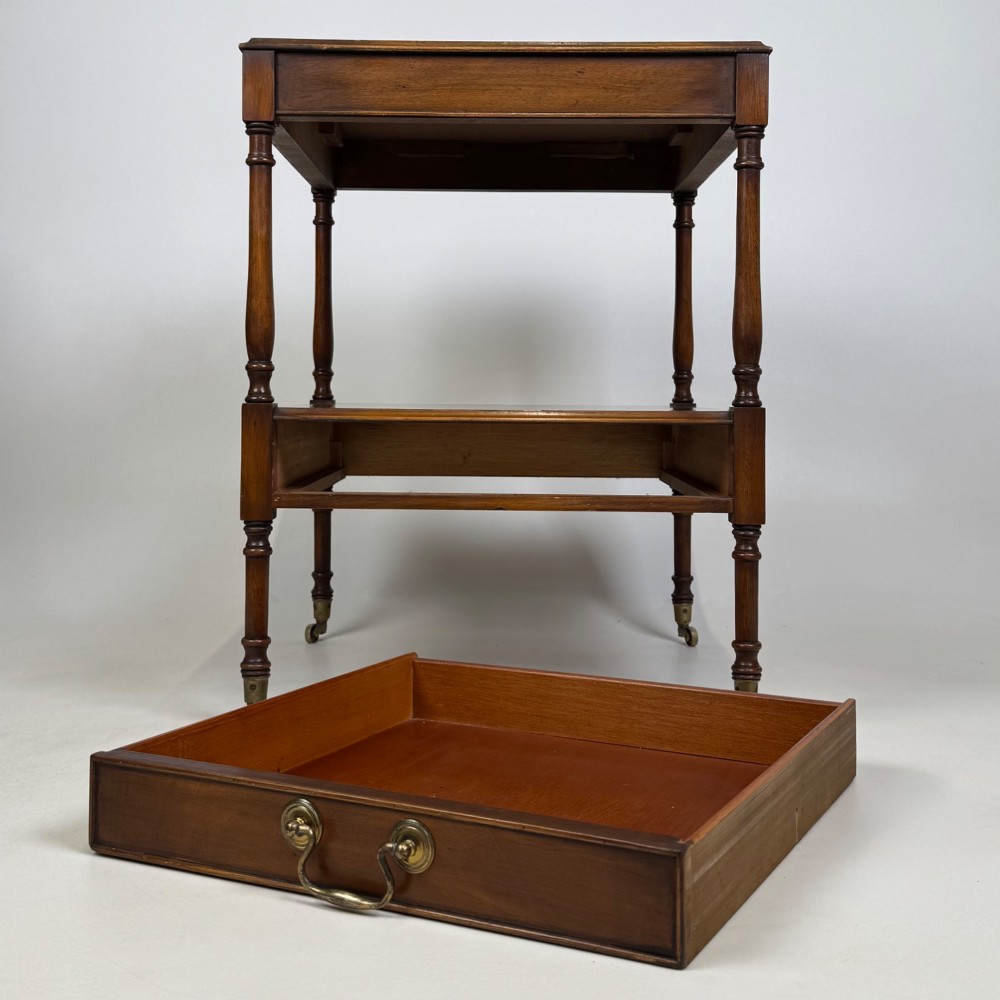 A pair of 20th-century warm mahogany bedside tables featuring turned support pillars, open middle shelves, single lower drawers with brass handles, and brass castors. View X